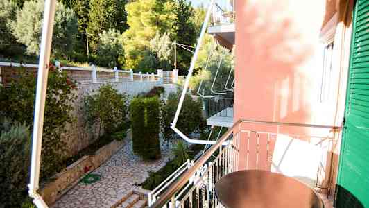 Balkong med bord som vetter mot en trädgård med stenlagd gång och grönska. (AI-genererad text)