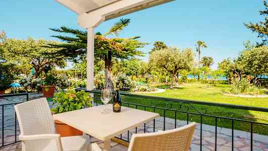 Uteservering med bord och stolar framför en grönskande trädgård. (AI-genererad text)