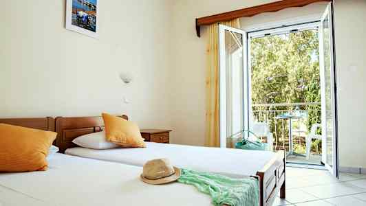 Ett hotellrum med enkelsängar, öppet fönster och utsikt mot balkong. (AI-genererad text)