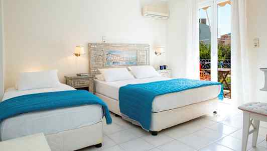 Ett hotellrum med två sängar bäddade med blåa täcken och vita lakan. En glasdörr leder till en balkong. (AI-genererad text)