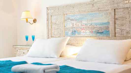 Dubbelbädd med vita kuddar, blå överkast och en vägglampa. (AI-genererad text)