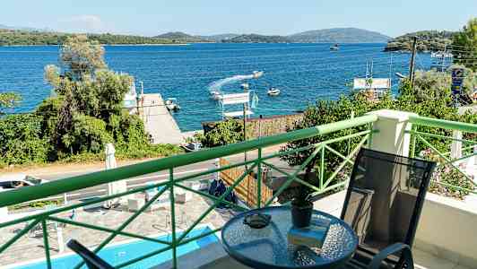 Utsikt från en balkong mot en blå havsvik med båtar och grönskande omgivningar. (AI-genererad text)