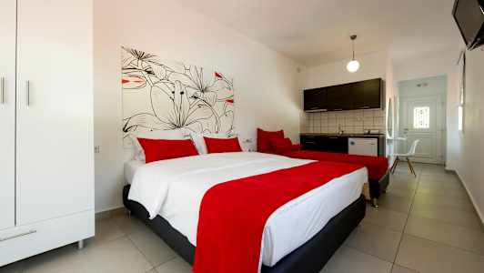 Ett hotellrum med två sängar har röda överkast och kuddar, en garderob till vänster och ett kök med mörka skåpsluckor i bakgrunden. (AI-genererad text)