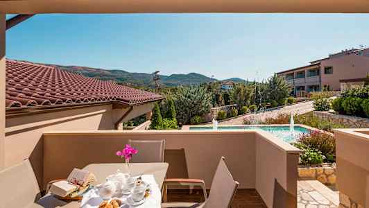 Utsikt från en terrass med bord och stolar, med en trädgård och fontän i bakgrunden. (AI-genererad text)