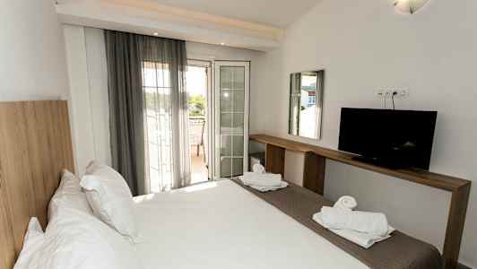 Ett hotellrum med en dubbelsäng, en TV på en träbänk, och en balkong med utsikt. (AI-genererad text)