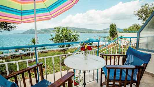 Uteplats med bord, stolar och en färgglad parasoll, med utsikt över havet och landskapet. (AI-genererad text)