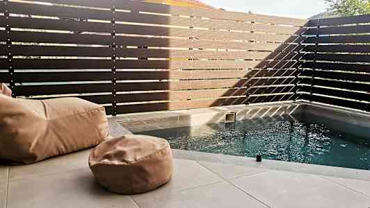 Liten pool med beige sittsäckar på en stenyta, omgiven av ett högt, mörkt staket. (AI-genererad text)