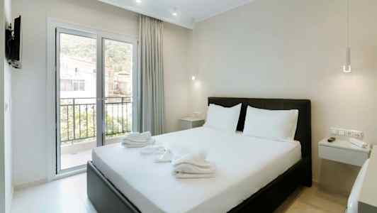 Ett hotellrum med en dubbelsäng, vita sängkläder och ett fönster som vetter mot en balkong. (AI-genererad text)