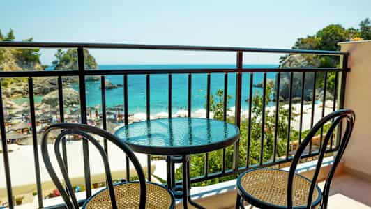 En balkong med ett bord och två stolar, med utsikt över havet och en strand. (AI-genererad text)