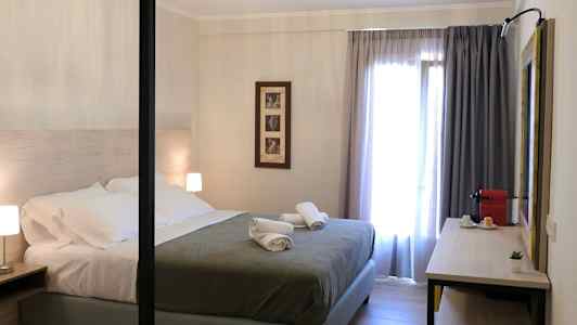 Modernt inrett sovrum med dubbelsäng, sängbord och en skrivbordsyta med kaffemaskin. (AI-genererad text)