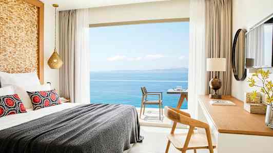 Ett hotellrum med en bäddad säng, skrivbord och utsikt över havet genom fönstret. (AI-genererad text)