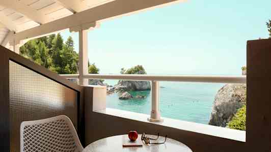 Utsikt från en balkong mot havet med klippor och träd. (AI-genererad text)