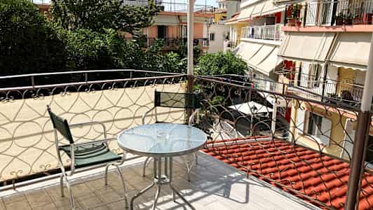 Balkong med glasbord och två metallstolar, med utsikt över grönska och omgivande byggnader. (AI-genererad text)