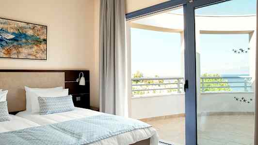 Bild på sovrum med dubbelsäng och öppen balkongdörr mot havsutsikt. (AI-genererad text)