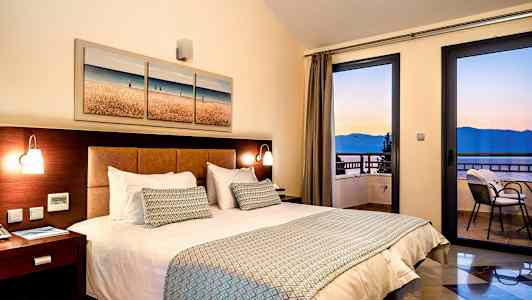 Rum med dubbelsäng, sängbord och havsutsikt genom fönster. (AI-genererad text)