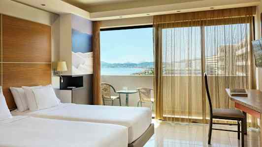 Rum med två enkelsängar, en balkong med utsikt över havet och sittmöbler. (AI-genererad text)