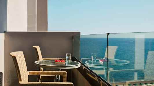 Utsikt från en balkong med två stolar och ett bord med ett glas vatten och en bok framför havet. (AI-genererad text)