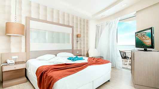 Hotellrum med stor säng och utsikt över balkong. (AI-genererad text)