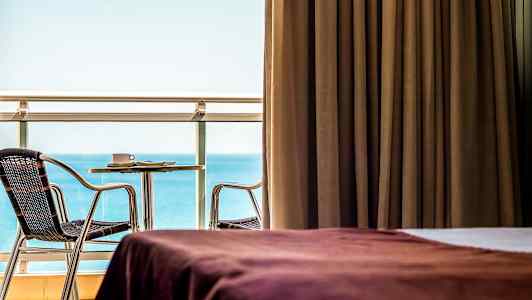 Rum med brun gardin, utsikt mot havet samt möblerad balkong. (AI-genererad text)