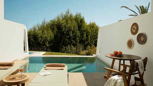 Uteplats med två solstolar, ett bord med dryck och bok, samt en pool med träd i bakgrunden. (AI-genererad text)