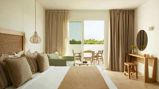 Ett hotellrum med en dubbelsäng, en sittgrupp, ett skrivbord och en utgång till en balkong. (AI-genererad text)