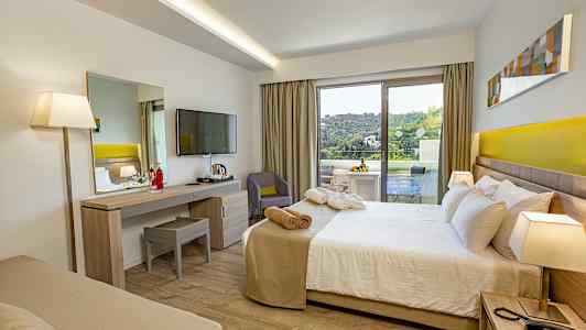 Ett hotellrum med säng, skrivbord, TV, och en balkong som visar en grön utsikt. (AI-genererad text)