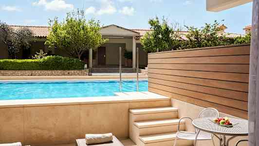 Utsikt från en terrass med solstolar och ett bord med frukt, mot en pool och trädgård. (AI-genererad text)