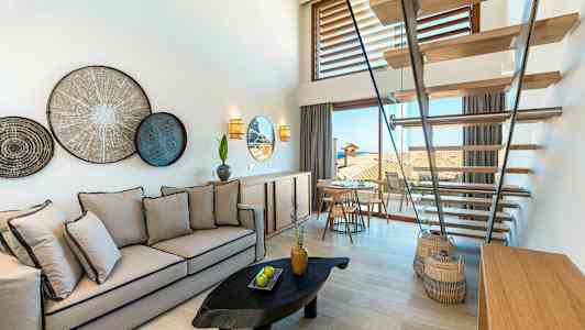 Ett ljus och stilrent rum med en soffa, ett trappsystem, väggdekorationer och utsikt mot en terrass. (AI-genererad text)