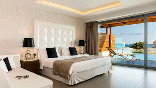 Ett hotellrum med dubbelsäng, dagsäng och utsikt mot en terrass med pool och hav. (AI-genererad text)