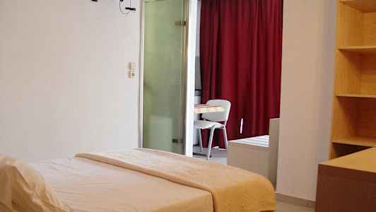 Ett hotellrum med en säng, ett bord och stolar, samt en hylla och röda gardiner. (AI-genererad text)