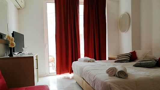 Ett hotellrum med en dubbelsäng, röda gardiner och en tv på en byrå. (AI-genererad text)