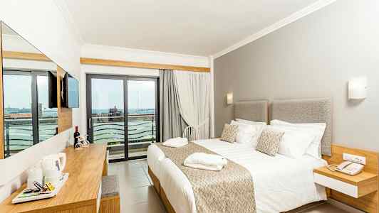 Ett hotellrum med en stor säng, ljusa möbler, och en balkong med utsikt. (AI-genererad text)