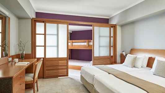 Bild av ett hotellrum med dubbelsäng, skrivbord och en sovalkov med våningssäng bakom träskjutdörrar. (AI-genererad text)