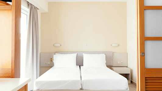 Två enkelsängar med vita sängkläder och neutrala möbler. (AI-genererad text)