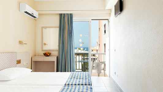 Hotellrum med två sängar, blågula sängöverkast, spegel, och en balkongdörr med utsikt. (AI-genererad text)