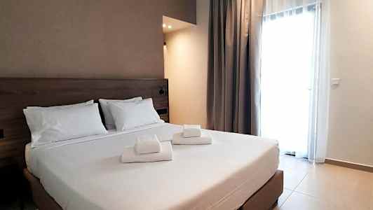 Ett hotellrum med en dubbelsäng och vita lakan, samt vikta handdukar placerade på sängen. (AI-genererad text)