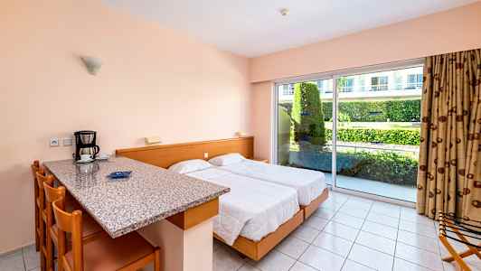 Ett hotellrum med två sängar, köksbar med sittplatser och stor glasdörr mot en trädgård. (AI-genererad text)