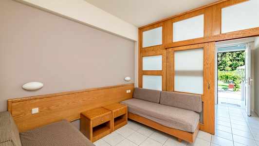 Ett rum med två enkelsängar och möbler i trä, öppnar upp mot en trädgård. (AI-genererad text)