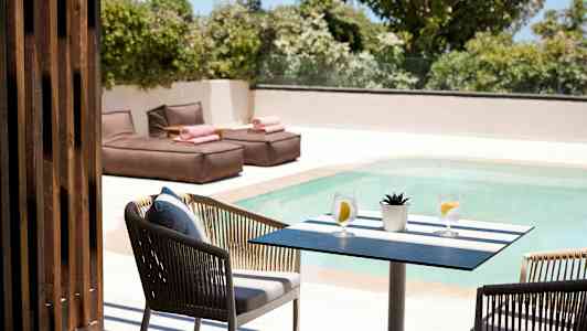 Ett bord med två glas vatten och en liten växt vid en pool, med solstolar i bakgrunden. (AI-genererad text)