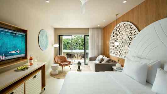 Ett elegant hotellrum med en stor säng, sittgrupp och en balkong med utsikt över grönska. (AI-genererad text)