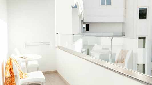 Vit balkong med glasräcke, ett bord och två stolar. (AI-genererad text)