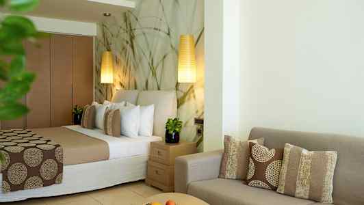 Ett hotellrum med en säng, soffgrupp och bord dekorerat med kuddar och frukt. (AI-genererad text)