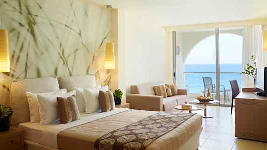 Hotellrum med havsutsikt och modern inredning inklusive säng, soffa och balkong. (AI-genererad text)