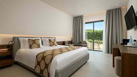 Ett hotellrum med en stor bäddad säng, sittgrupp och glasdörr mot terrass. (AI-genererad text)