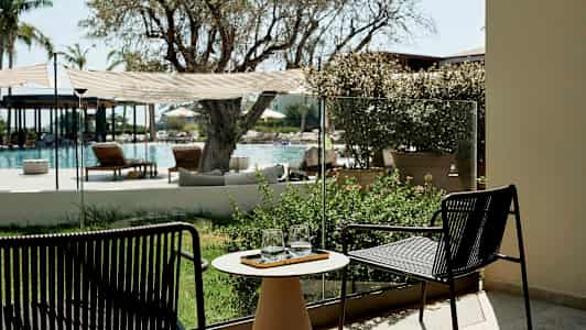 Utsikt mot en utomhuspool med stolar och växter i förgrunden. (AI-genererad text)