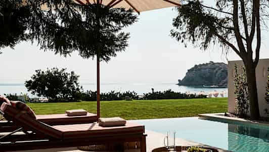 Solstolar vid en pool med utsikt mot havet och en klippa. (AI-genererad text)