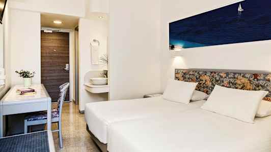 Ett hotellrum med två vita enkelsängar, ett skrivbord, en stol och en liten handfat utanför badrummet. (AI-genererad text)