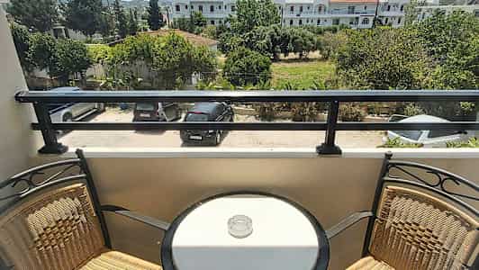 En balkong med två stolar och ett runt bord med en askkopp, med utsikt över en parkering och grönska. (AI-genererad text)