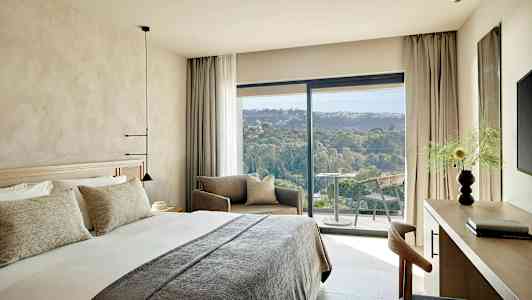 Ett modernt hotellrum med en stor säng, sittgrupp och en balkong med utsikt över ett grönt landskap. (AI-genererad text)