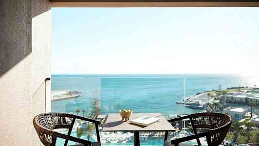 Två stolar och ett bord med en skål och en bok står på en balkong med utsikt över havet. (AI-genererad text)